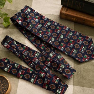 May include: A navy blue necktie featuring a repeating geometric pattern of small squares and diamonds in shades of red, green, white, and gold. The tie has a pointed end and a smooth, woven texture, displaying a consistent print across the entire fabric surface.