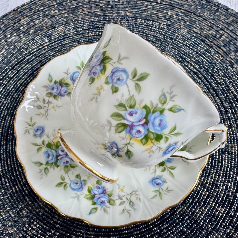 Pu&ograve; includere: Una tazza da t&egrave; e un piattino bianchi con un motivo floreale blu e giallo. La tazza e il piattino hanno un bordo dorato.