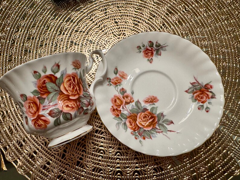 Pode incluir: Um conjunto de ch&aacute; branco com x&iacute;cara e pires com um design floral com rosas cor-de-rosa e laranja. O conjunto &eacute; decorado com uma delicada borda dourada.