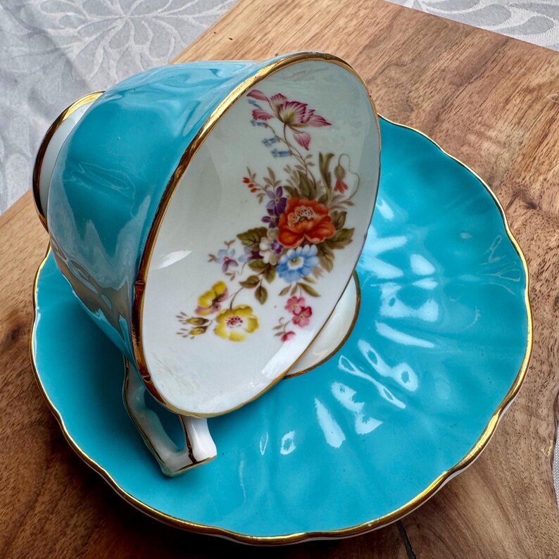 May include: A turquoise teacup and saucer set with a floral design. The cup and saucer have a gold trim.