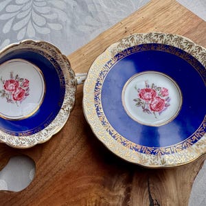 May include: A blue and gold teacup and saucer set with a floral design. The cup and saucer have a blue background with a gold rim and a floral pattern in the centre.