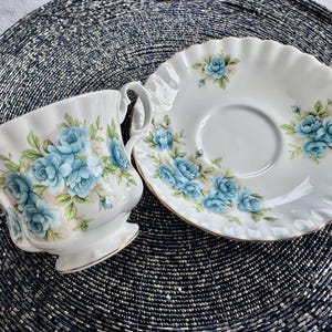 May include: A white teacup and saucer with a blue floral pattern. The cup and saucer have a scalloped edge and a gold trim.