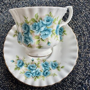 May include: A white teacup and saucer with a blue floral pattern. The cup and saucer have a gold trim around the edges.