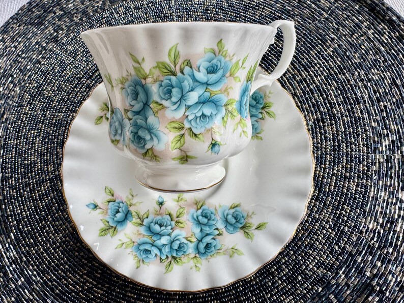May include: A white teacup and saucer with a blue floral pattern. The cup and saucer have a gold trim around the edges.