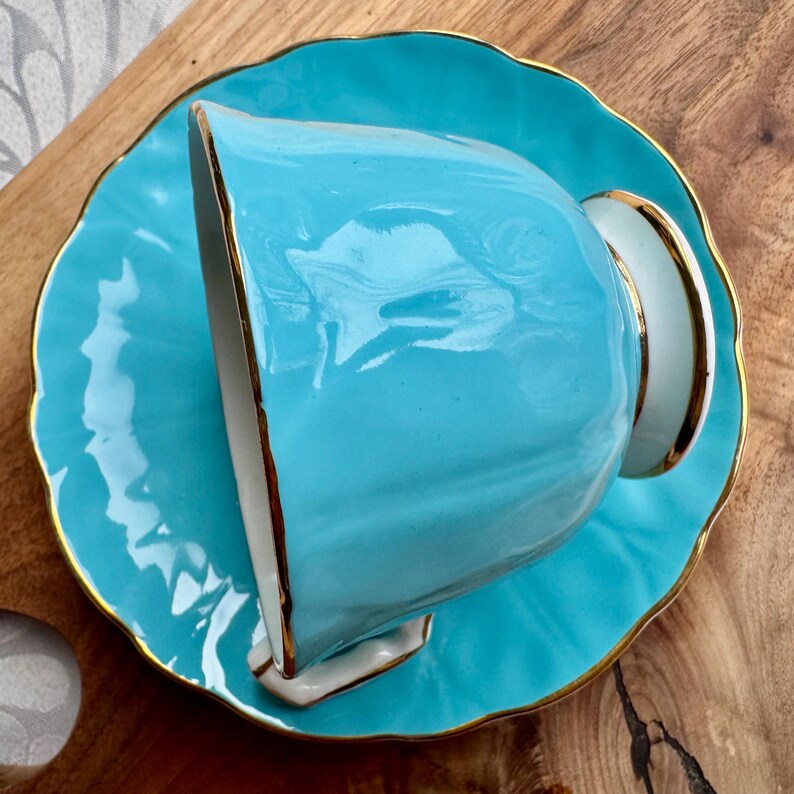 May include: A turquoise teacup and saucer set with a gold trim. The cup is upside down on the saucer.