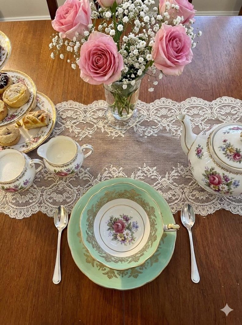 Peut inclure: Un service &agrave; th&eacute; comprenant une tasse et une soucoupe vert menthe avec des filigranes dor&eacute;s, une th&eacute;i&egrave;re blanche, un pot &agrave; lait et un sucrier &agrave; motifs floraux. Un vase en verre contient des roses roses et du gypsophile, avec des p&acirc;tisseries.