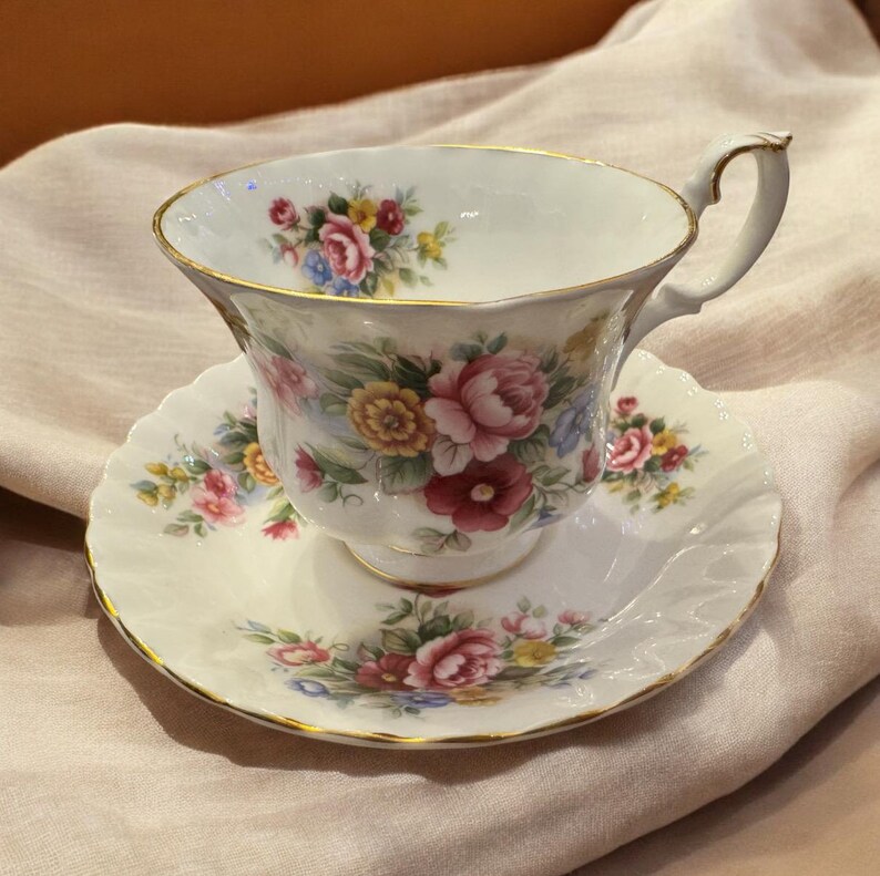 May include: A white teacup and saucer with a floral pattern. The cup has a gold rim and the saucer has a scalloped edge.