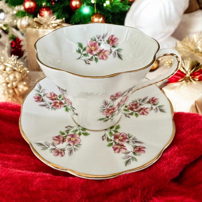 May include: A white teacup and saucer with a floral pattern. The cup and saucer have a gold trim and are decorated with pink flowers and green leaves.