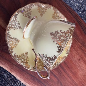 May include: A yellow teacup and saucer with gold trim and a floral pattern. The cup and saucer are on a wooden surface.