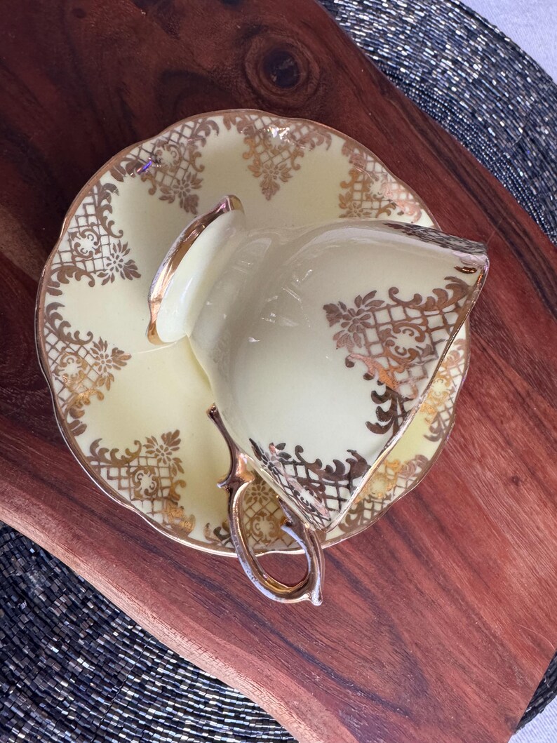 May include: A yellow teacup and saucer with gold trim and a floral pattern. The cup and saucer are on a wooden surface.