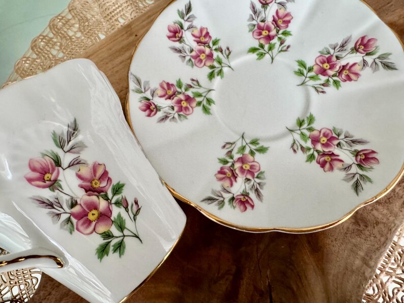 May include: A white teacup and saucer set with a delicate floral pattern. The set features pink and green flowers on a white background with a gold trim.