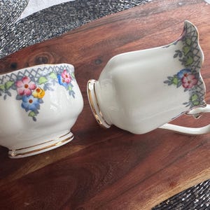 Pu&ograve; includere: Un set vintage di brocca per la panna e zuccheriera in porcellana con motivi floreali in tonalit&agrave; rosa, blu, giallo e verde. La porcellana &egrave; bianca con un bordo dorato.
