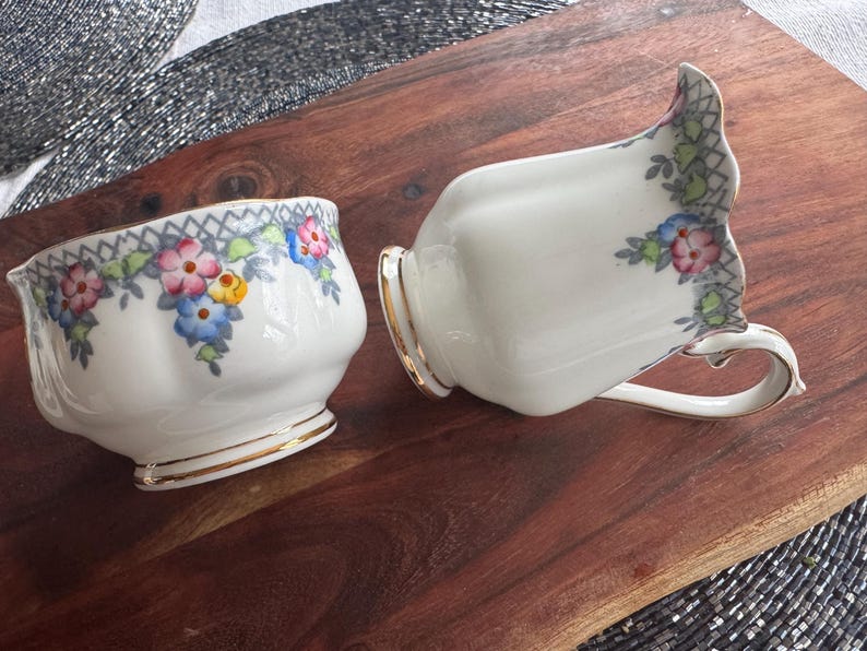 Pu&ograve; includere: Un set vintage di brocca per la panna e zuccheriera in porcellana con motivi floreali in tonalit&agrave; rosa, blu, giallo e verde. La porcellana &egrave; bianca con un bordo dorato.