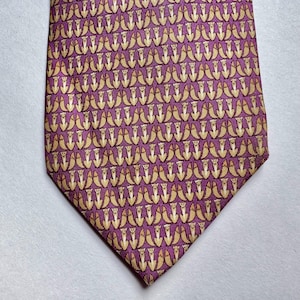 Puede incluir: Una corbata con un patr&oacute;n repetitivo de peque&ntilde;os zorros de color beige dispuestos en filas sobre un fondo morado vibrante. Los zorros est&aacute;n representados en posici&oacute;n sentada, creando un dise&ntilde;o gr&aacute;fico denso y uniforme en la tela.