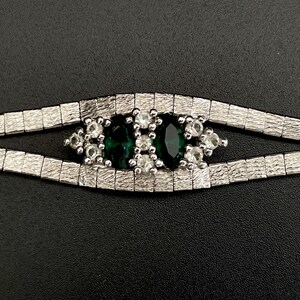 May include: A silver chain bracelet featuring a green and white stone centrepiece. The stone is surrounded by smaller white stones.