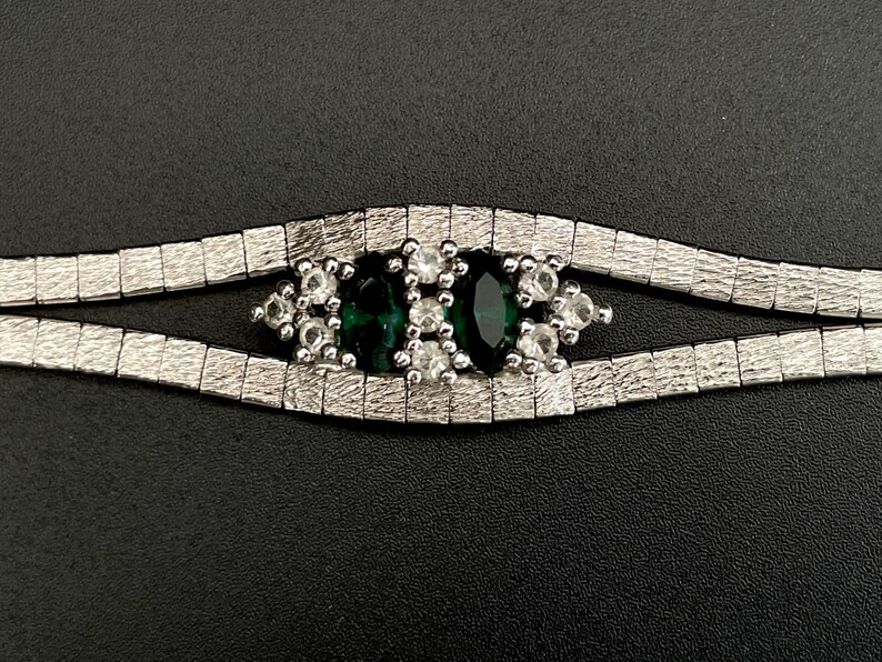 May include: A silver chain bracelet featuring a green and white stone centrepiece. The stone is surrounded by smaller white stones.