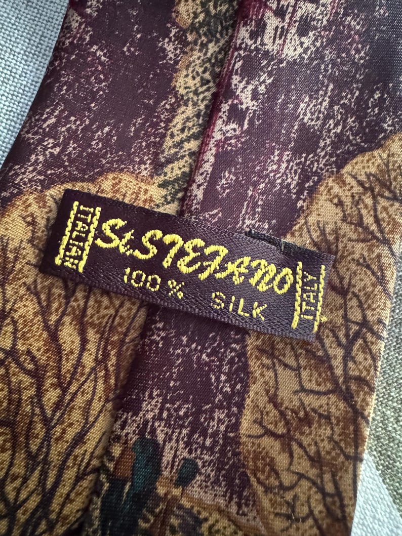 Pu&ograve; includere: Una cravatta in 100% seta con un motivo astratto bordeaux scuro e marrone con sagome di alberi. Un'etichetta rettangolare in tessuto &egrave; cucita sul retro, riportante il testo St. Stefano, 100% Silk e Italian.