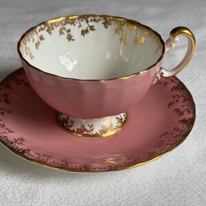 Peut inclure: Service &agrave; th&eacute; rose avec des bordures dor&eacute;es. La tasse a un int&eacute;rieur blanc et une anse dor&eacute;e. La soucoupe et la tasse sont d&eacute;cor&eacute;es de motifs floraux dor&eacute;s. L'ensemble est en porcelaine.
