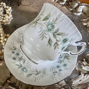 May include: White teacup and saucer set with a floral design in shades of blue and green. The teacup has a curved handle and a silver trim. The saucer has a matching floral pattern and silver trim. The set is placed on a silver tray.