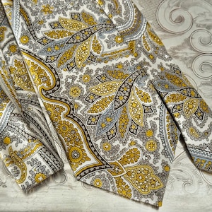 May include: A vintage paisley tie and matching pocket square. The tie features a repeating pattern of yellow, gray, and brown paisley shapes on a white background. The pocket square is folded and visible next to the tie.
