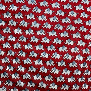 Puede incluir: Una corbata roja con un patr&oacute;n repetitivo de peque&ntilde;os elefantes blancos con orejas de color azul claro. La tela tiene una textura acanalada diagonal visible en toda la superficie, creando un dise&ntilde;o consistente y uniforme.