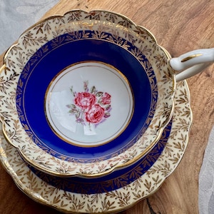 May include: A vintage teacup and saucer set with a cobalt blue rim and gold floral pattern. The cup features a delicate floral design in the centre.