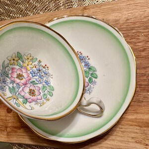 May include: A vintage teacup and saucer set with a green and white floral pattern. The cup and saucer have a gold trim around the edges.