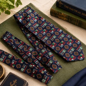 May include: A navy blue necktie featuring a repeating geometric pattern of red, green, and white shapes. The tie displays a series of small, intricate motifs arranged in a grid, with a pointed end and a smooth, woven texture throughout the fabric.
