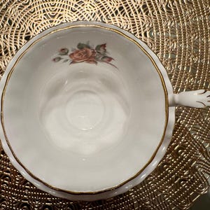Pode incluir: Uma ch&aacute;vena de ch&aacute; branca com uma borda dourada e um desenho floral. A ch&aacute;vena de ch&aacute; tem uma pega com a forma de uma m&atilde;o.