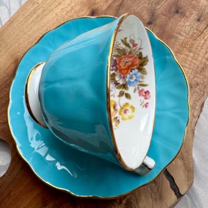 May include: A turquoise teacup and saucer set with a floral pattern and gold trim.
