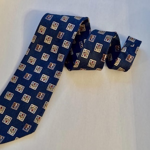 May include: A dark blue necktie featuring a repeating pattern of small, light-colored squares. Each square contains a detailed, centered graphic element with red and gold accents. The tie has a textured, woven appearance throughout the fabric.
