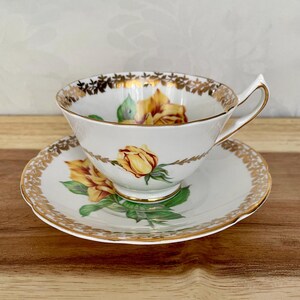 Puede incluir: Juego de taza y platillo blancos con dise&ntilde;o de rosa amarilla. La taza y el platillo tienen ribete dorado y un delicado estampado floral. La taza tiene un asa curvada y se asienta sobre un platillo a juego, creando un elegante juego de t&eacute;.