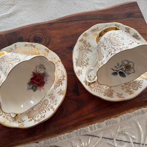 May include: Two vintage teacups and saucers with gold trim and floral patterns. The cups have a white background with gold accents and floral designs. The saucers have a similar design with a white background and gold accents.