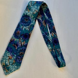 Pode incluir: Uma gravata com um padr&atilde;o floral vibrante em tons de azul profundo, verde-azulado e verde. O design consiste em motivos florais estilizados e sobrepostos com centros escuros e detalhes de p&eacute;talas em espiral por todo o tecido.