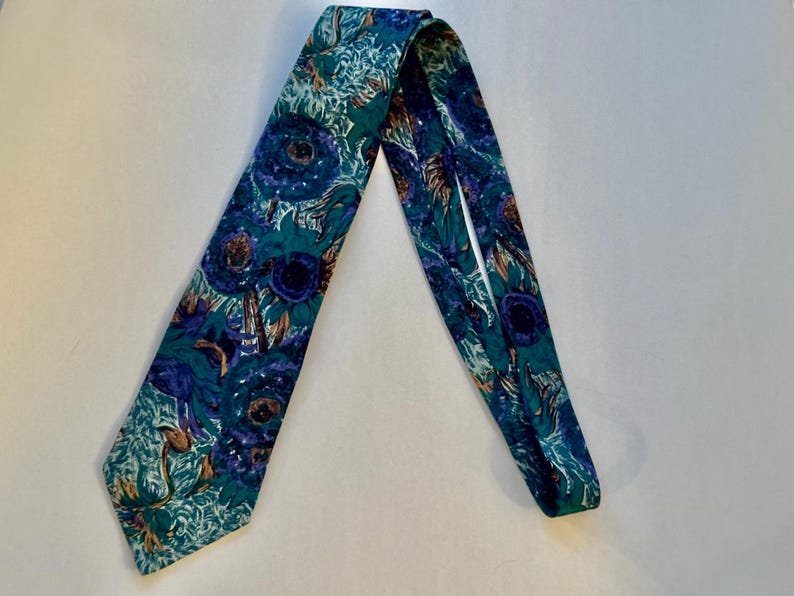 Pode incluir: Uma gravata com um padr&atilde;o floral vibrante em tons de azul profundo, verde-azulado e verde. O design consiste em motivos florais estilizados e sobrepostos com centros escuros e detalhes de p&eacute;talas em espiral por todo o tecido.
