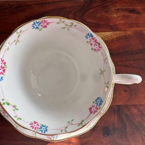 May include: A white teacup and saucer with a gold rim and floral pattern in pink, blue, and green.