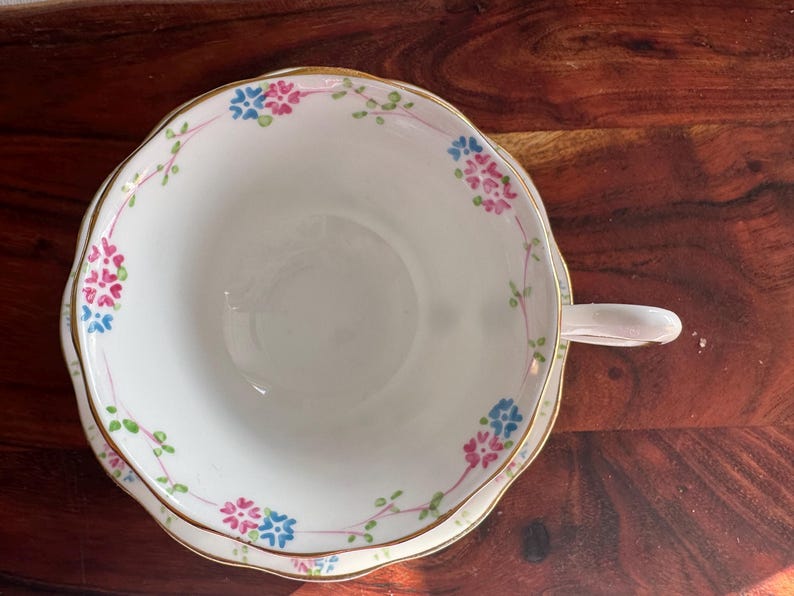 May include: A white teacup and saucer with a gold rim and floral pattern in pink, blue, and green.