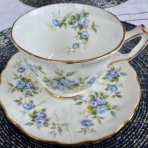 Pu&ograve; includere: Una tazza da t&egrave; e un piattino bianchi con un delicato motivo floreale blu. La tazza e il piattino hanno un bordo dorato.
