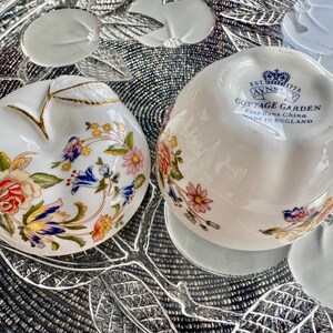 K&ouml;nnte beinhalten: Zwei wei&szlig;e, apfelf&ouml;rmige Keramikgerichte mit Blumendesigns. Das untere Gericht tr&auml;gt den Text "EST. 1773 AYNSLEY COTTAGE GARDEN Fine Bone China MADE IN ENGLAND".