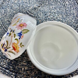 K&ouml;nnte beinhalten: Eine wei&szlig;e Zuckerdose aus Keramik mit einem Deckel mit Blumendesign. Der Deckel zeigt ein Blumenmuster mit rosa, blauen, gelben und gr&uuml;nen Blumen. Die Sch&uuml;ssel ist leer.