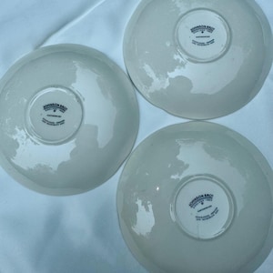 Puede incluir: Tres platillos de cer&aacute;mica blanquecina. Cada platillo tiene el texto "JOHNSON BROS ENGLAND 1883 EARTHENWARE" impreso en la base. Los platillos est&aacute;n colocados sobre una superficie blanca, resaltando su dise&ntilde;o cl&aacute;sico.