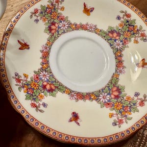 May include: A white porcelain saucer with a gold rim and a floral design featuring butterflies. The saucer has a central well for a teacup.