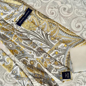 May include: A Banana Republic tie with a paisley pattern in shades of yellow, gray, and white. The tie is made in the USA and features the brand's label.