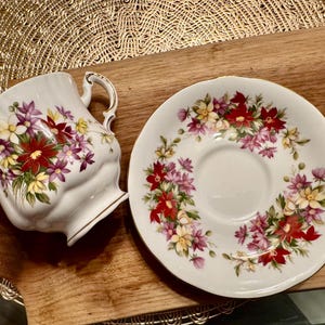 May include: A white teacup and saucer with a floral pattern. The pattern features red, pink, yellow, and green flowers on a white background.