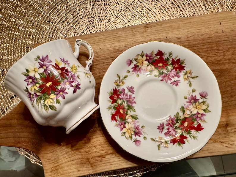 May include: A white teacup and saucer with a floral pattern. The pattern features red, pink, yellow, and green flowers on a white background.