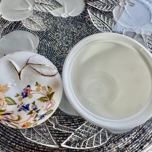 K&ouml;nnte beinhalten: Eine wei&szlig;e Porzellan-Zuckerdose mit Deckel und floralem Design. Der Deckel hat einen goldenen Rand und die Dose ein Blumenmuster mit rosa, blauen und gelben Blumen.