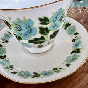 May include: A white teacup and saucer with a gold rim and a floral pattern in shades of blue and green.