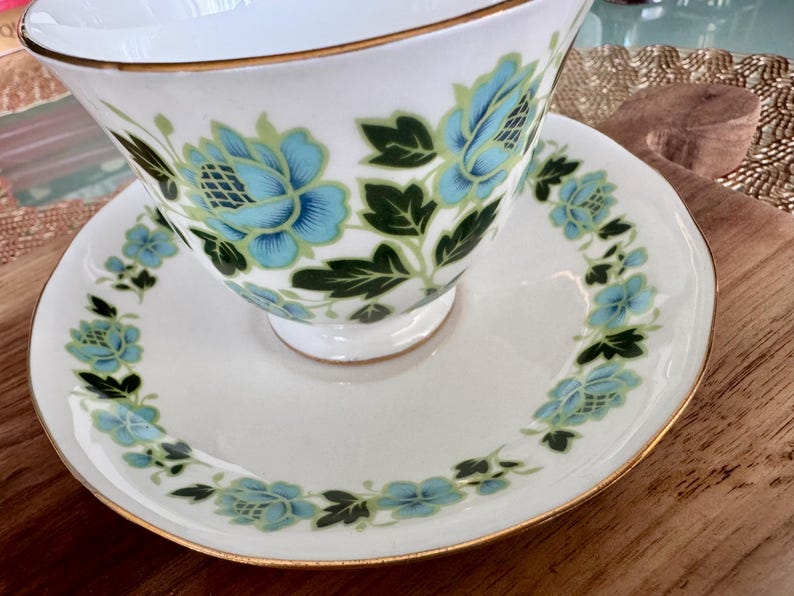May include: A white teacup and saucer with a gold rim and a floral pattern in shades of blue and green.