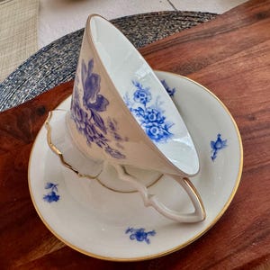 May include: A white teacup and saucer with a blue floral pattern. The teacup has a delicate handle and the saucer has a gold rim.