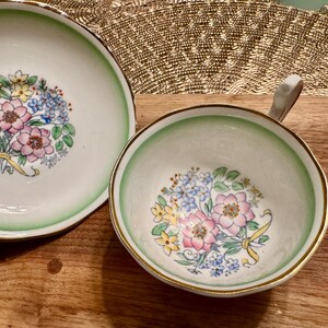May include: A vintage teacup and saucer set with a green and white floral design. The floral pattern features pink, yellow, and blue flowers.